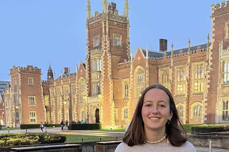 student standing  smiling to camera with Queen's University in background